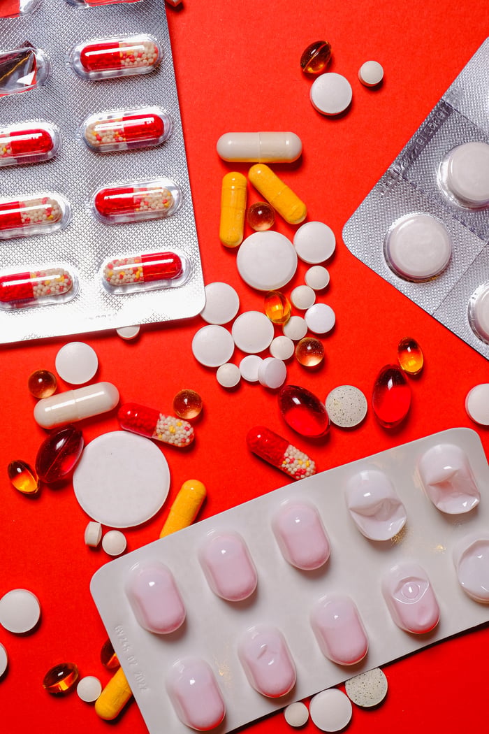 Colorful assortment of pills and tablets spread across a vibrant orange background.