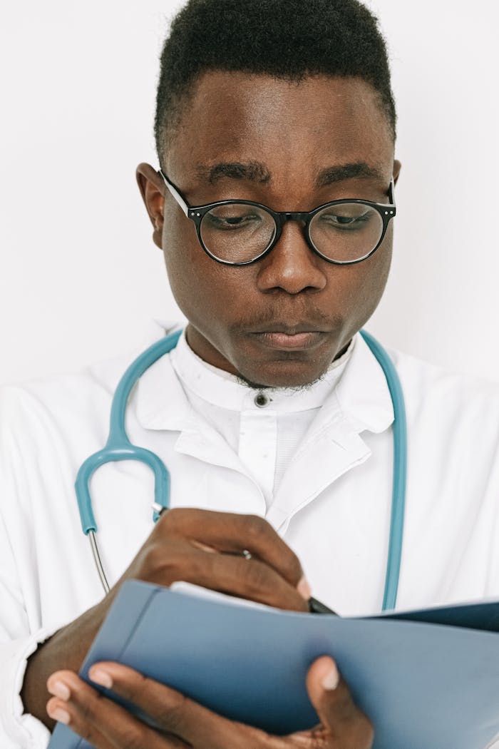 Focused male doctor with stethoscope writing notes on clipboard indoors.